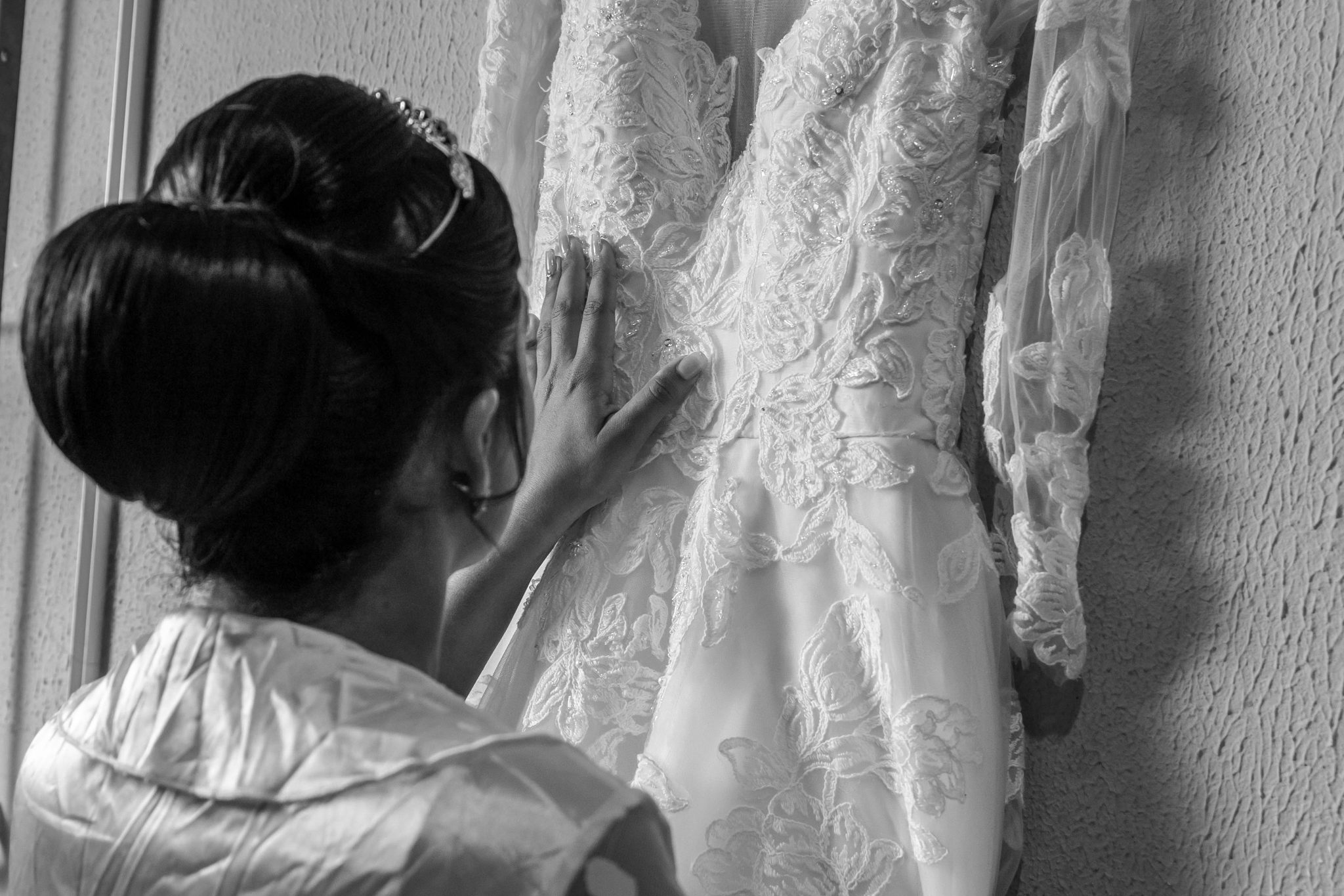 Black and white image of a bride admiring her intricate lace wedding gown, capturing the essence of anticipation.