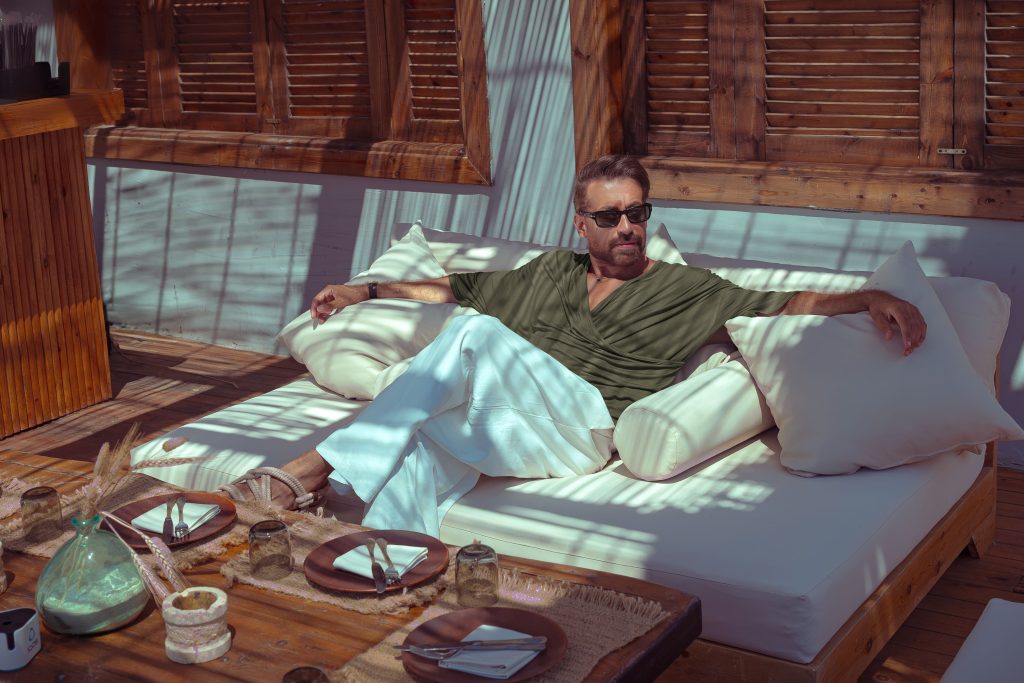 Man relaxing on an outdoor lounge, surrounded by sunlight and wooden textures.