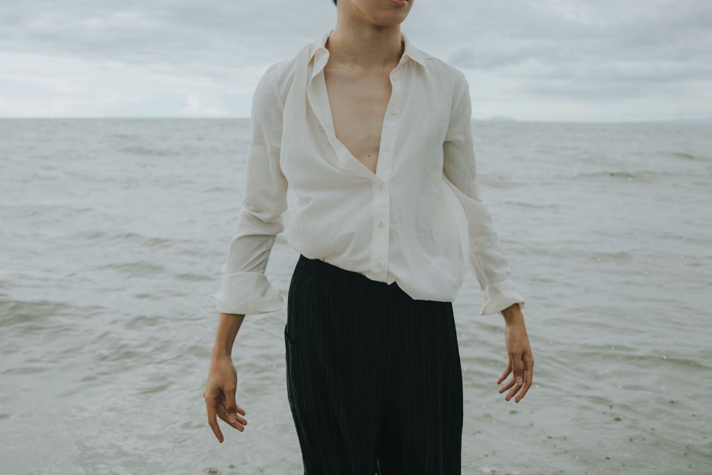 Person standing by the seaside in elegant attire, embracing the ocean breeze.